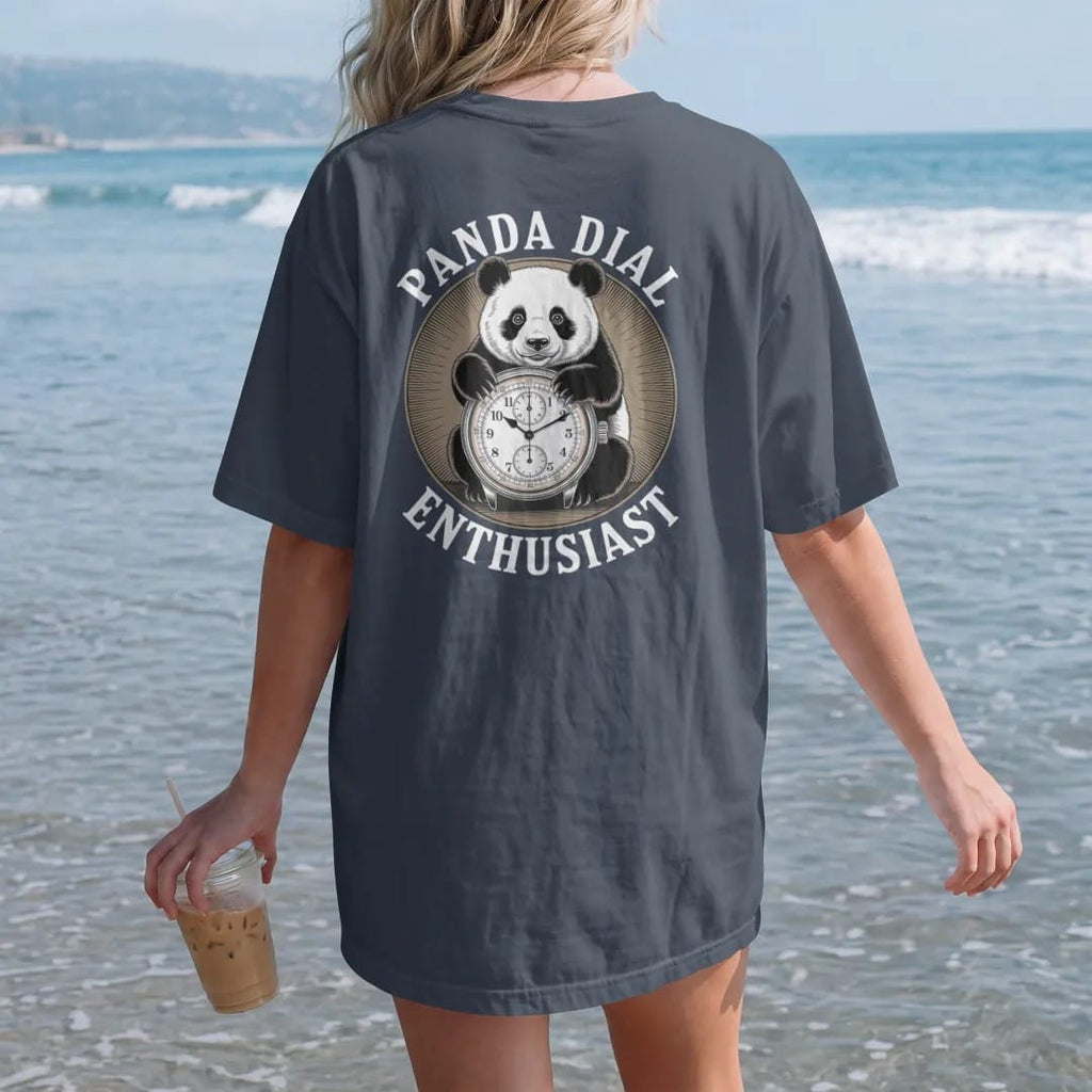 Woman on the beach in a Midnight tee, back view: a cute panda hugging a chronograph with contrasting subdials, under Panda Dial and Enthusiast, as a fine engraving in antique gold and cream.