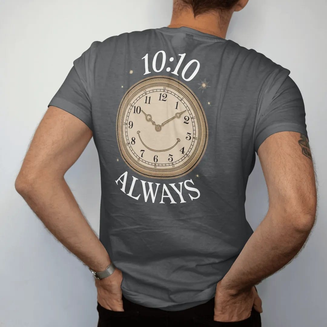 Man wearing a Graphite tee, seen from the back: a large watch dial with hands at ten past ten forming a smile, with 10:10 in dial numerals and Always below, as a fine engraving in antique gold and cream.