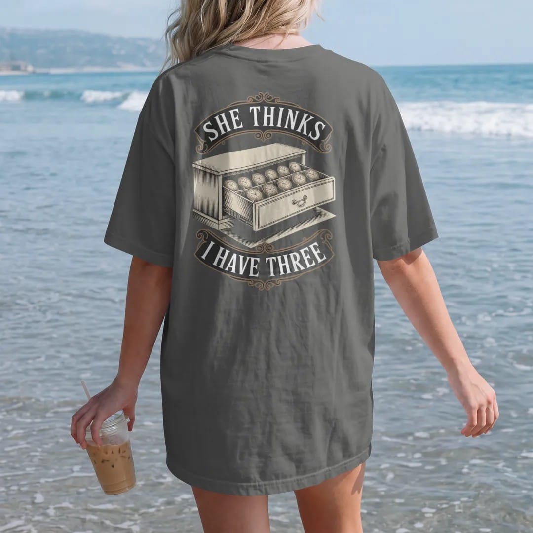 Woman on the beach in a Pepper tee, back view: a drawer open just enough to reveal a long row of hidden watches with a shushing finger icon, under She Thinks and I Have Three, as a fine engraving in antique gold and cream.