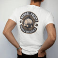 Man wearing a White tee, seen from the back: a round distillery badge with an engraved oak barrel and wheat sprigs, with "BARREL PROOF" and "UNCUT & UNFILTERED" in condensed Victorian display capitals, printed as a fine engraving in antique gold…