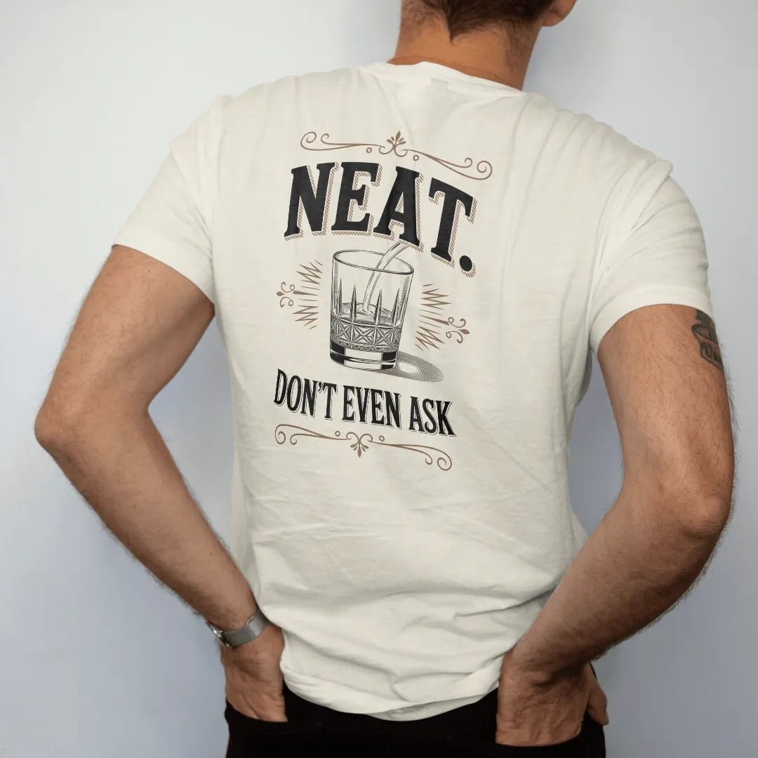 Man wearing a Ivory tee, seen from the back: an oversized serif word over a small crystal rocks glass, with "NEAT." and "DON'T EVEN ASK" in heavy high-contrast Didone serif with small engraved caps, printed as a fine engraving in oxblood, charred…