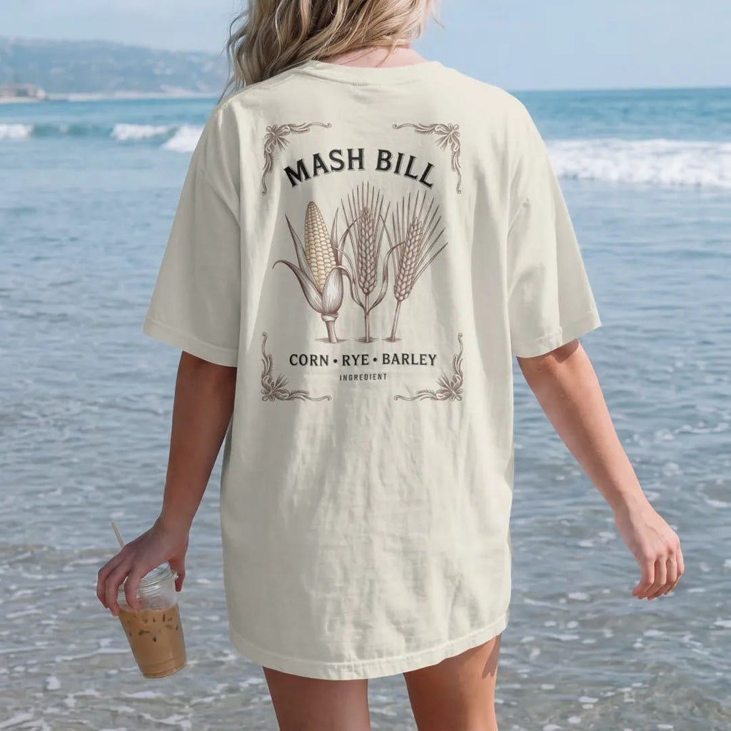 Woman on the beach in a Ivory tee, back view: three engraved grain stalks of corn, rye and barley on a recipe card, with "MASH BILL" and "CORN · RYE · BARLEY", printed as a fine engraving in antique gold and warm cream.