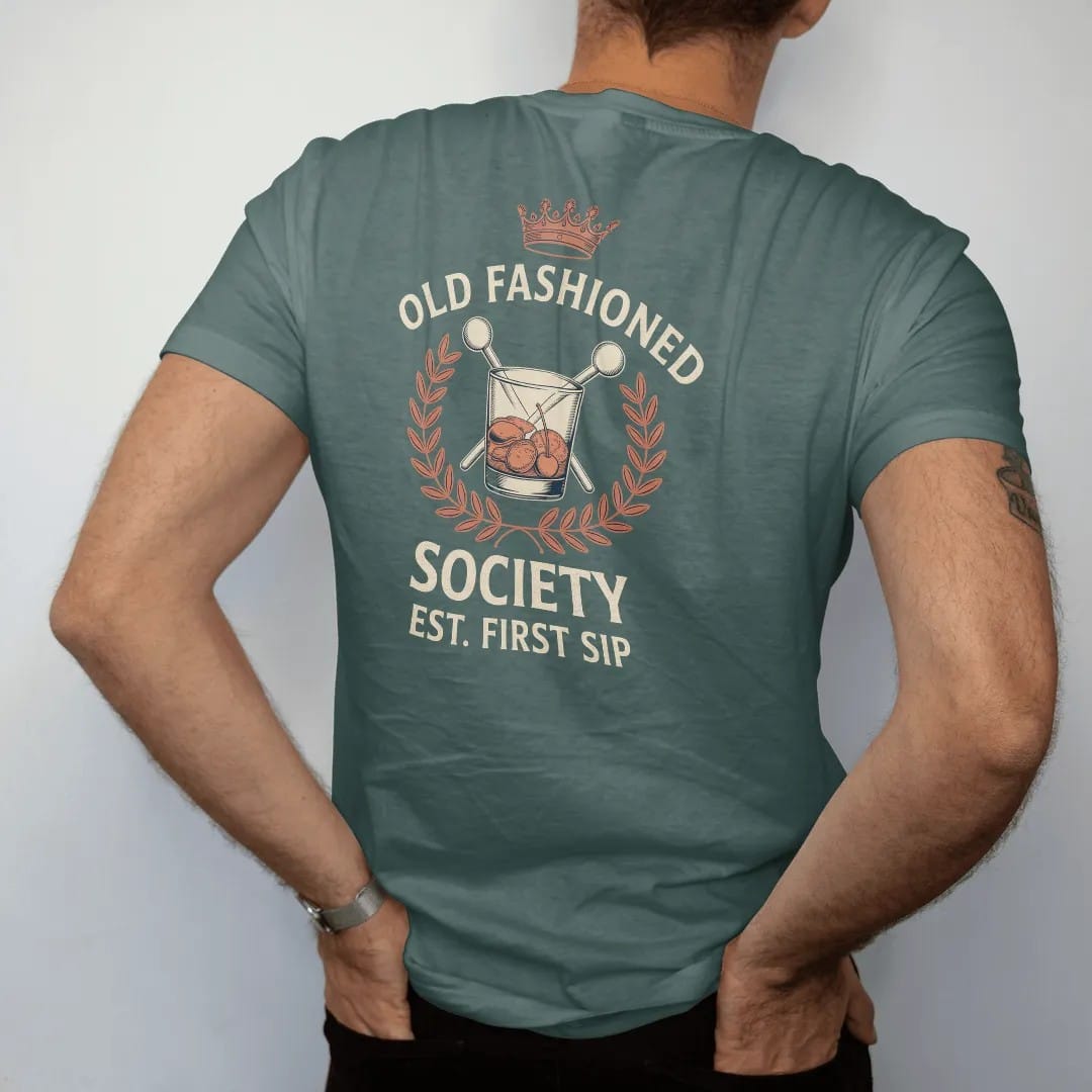 Man wearing a Blue Spruce tee, seen from the back: a members-club crest with an Old Fashioned glass and crossed muddlers, with "OLD FASHIONED", "SOCIETY" and "EST. FIRST SIP" in engraved serif small caps with a Didone headline, printed as a fine…