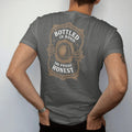 Man wearing a Pepper tee, seen from the back: a guilloche-engraved tax-strip emblem with a barrel icon, with "BOTTLED IN BOND" and "100 PROOF HONEST", printed as a fine engraving in antique gold and warm cream.