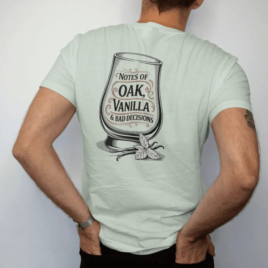 Man wearing a Bay tee, seen from the back: a glencairn glass with swirling aroma wisps, with "NOTES OF", "OAK, VANILLA" and "& BAD DECISIONS", printed as a fine engraving in oxblood, charred oak brown and antique gold.