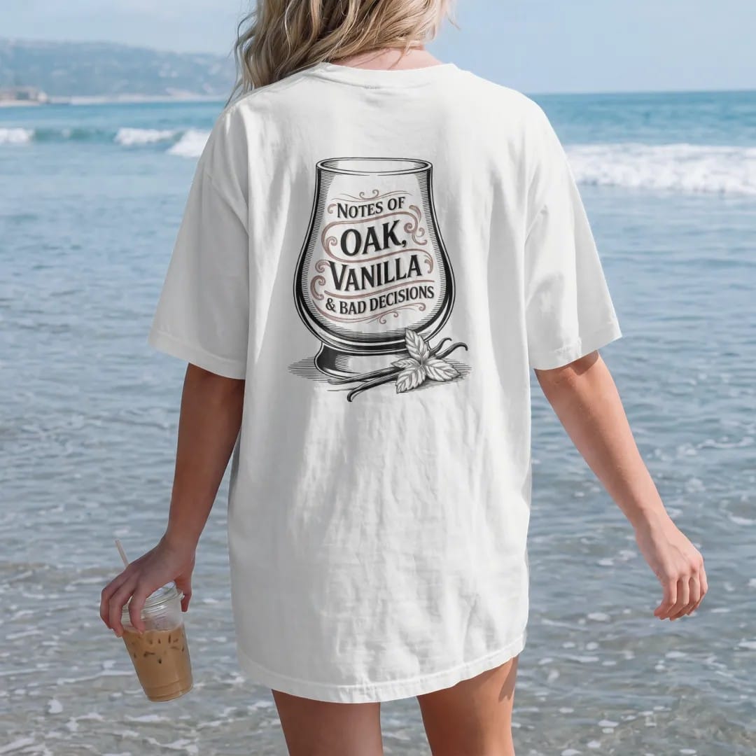 Woman on the beach in a White tee, back view: a glencairn glass with swirling aroma wisps, with "NOTES OF", "OAK, VANILLA" and "& BAD DECISIONS", printed as a fine engraving in oxblood, charred oak brown and antique gold.