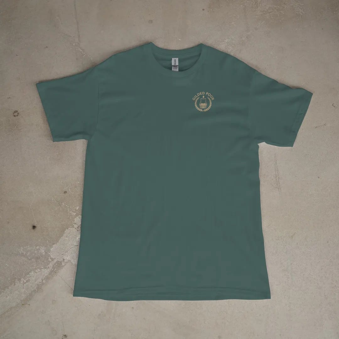 Front of a Blue Spruce tee laid flat, with the small Gilded Pour logo on the left chest.