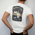 Man wearing a White tee, seen from the back: a coupe with a cherry beside a mixing glass and bar spoon, with "MANHATTAN" and "STIRRED, NEVER SHAKEN" in Art Deco high-contrast serif capitals, printed as a fine engraving in antique gold and warm cream.