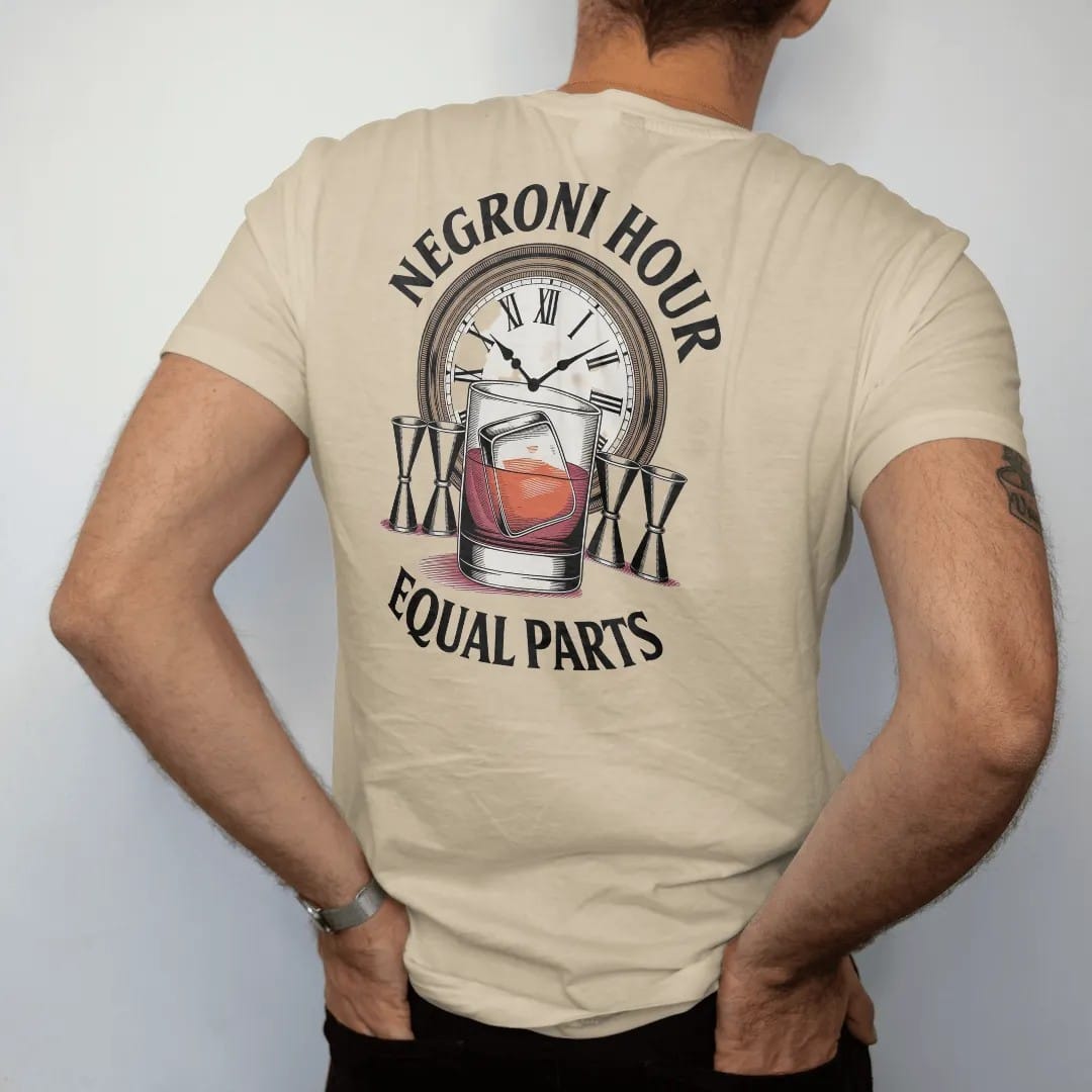 Man wearing a Sandstone tee, seen from the back: a Negroni glass with orange wheel, three jiggers and a clock face, with "NEGRONI HOUR" and "EQUAL PARTS", printed as a fine engraving in oxblood, charred oak brown and antique gold.