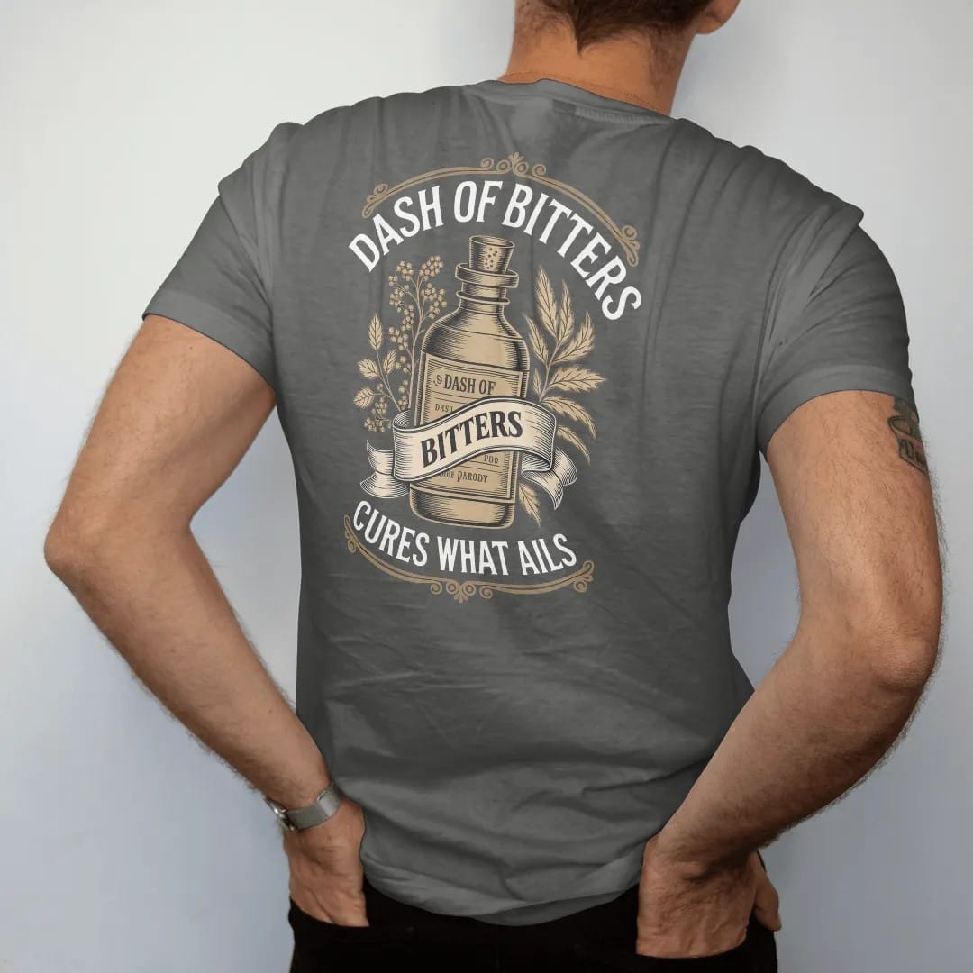 Man wearing a Pepper tee, seen from the back: a paper-wrapped bitters bottle among engraved herbs, with "DASH OF BITTERS" and "CURES WHAT AILS" in Victorian apothecary display serif, printed as a fine engraving in antique gold and warm cream.