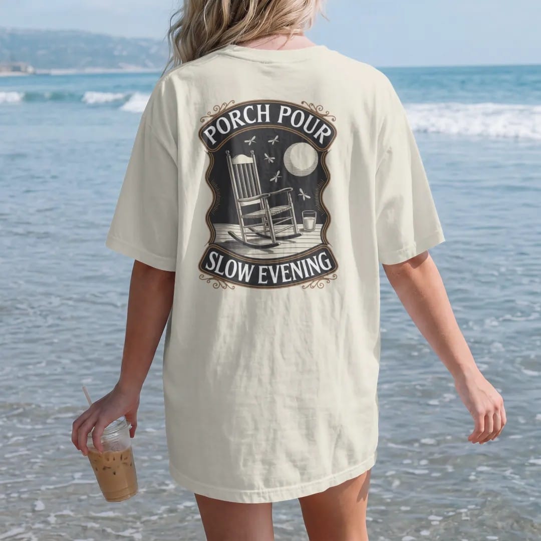 Woman on the beach in a Ivory tee, back view: a rocking chair on a porch with a glass on the armrest under a low moon, with "PORCH POUR" and "SLOW EVENING" in warm Victorian serif capitals, printed as a fine engraving in antique gold and warm cream.