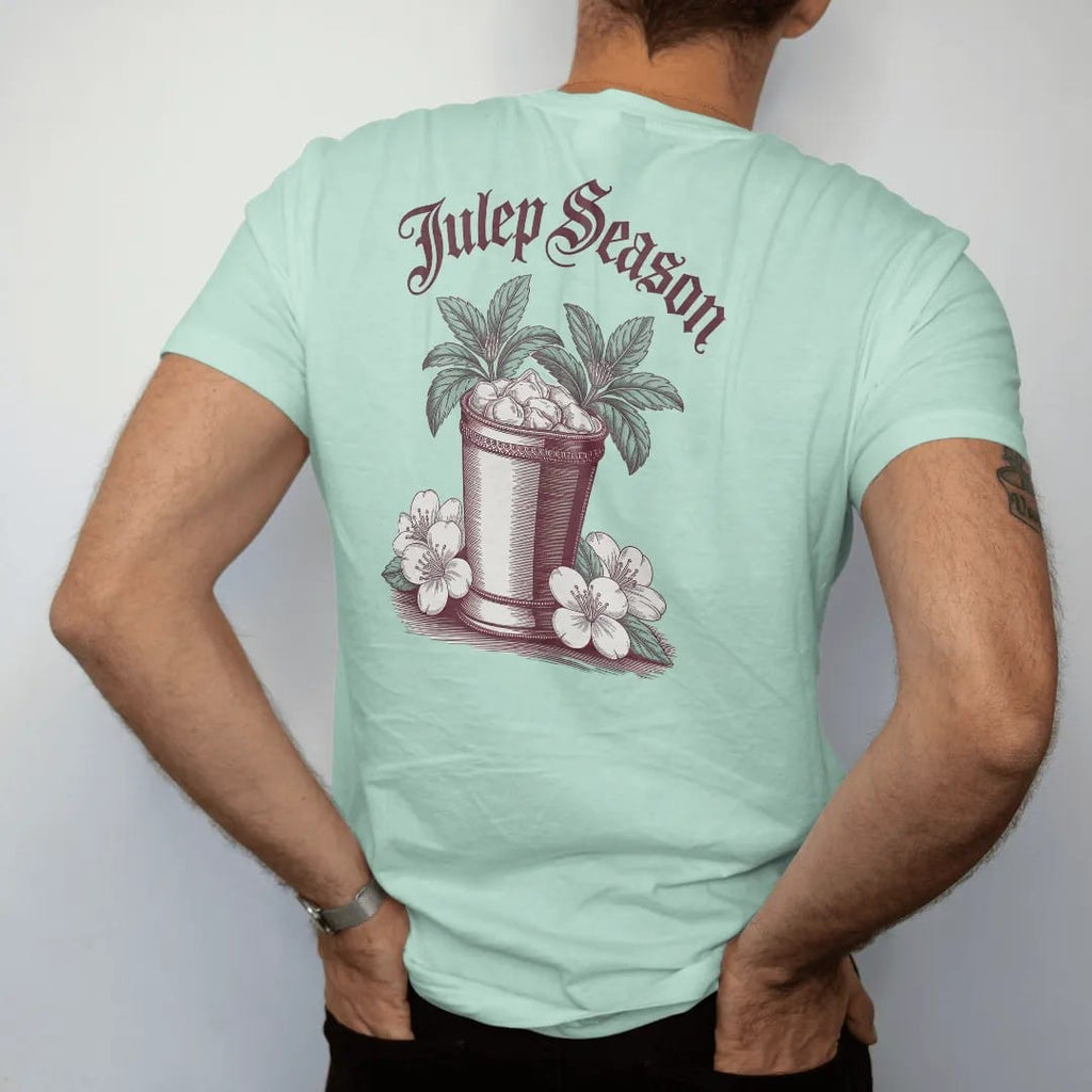 Man wearing a Chalky Mint tee, seen from the back: a silver julep cup overflowing with mint among spring blossoms, with "JULEP SEASON", printed as a fine engraving in oxblood, charred oak brown and antique gold.