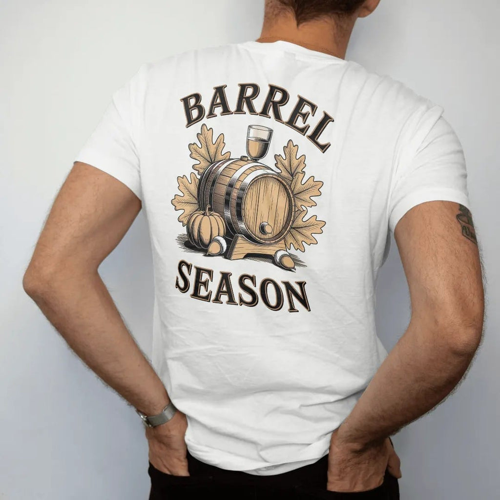 Man wearing a White tee, seen from the back: an oak barrel with autumn leaves, acorns and a pumpkin, with "BARREL SEASON" in warm Victorian serif capitals, printed as a fine engraving in antique gold and warm cream.
