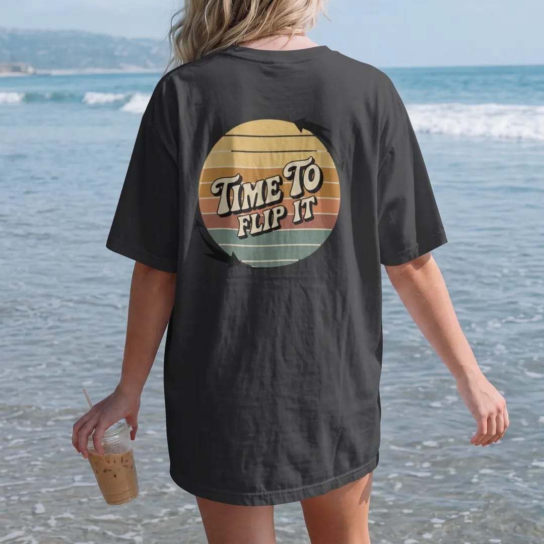 Woman on the beach in a Black tee, back view: a record flipping mid-air with motion arrows, with "TIME TO" and "FLIP IT" in chunky 70s lettering and small 70s caps, printed in faded, cracked cream, mustard, burnt orange and faded teal over faded…