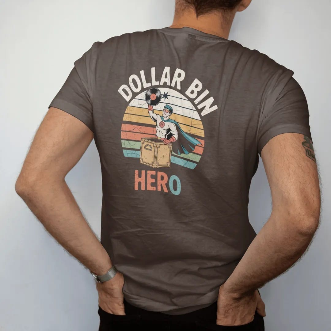 Man wearing a Espresso tee, seen from the back: a caped crate digger holding a record aloft over a cardboard bin, with "DOLLAR BIN" and "HERO" in chunky 70s lettering and small 70s caps, printed in faded, cracked cream, mustard, burnt orange and…