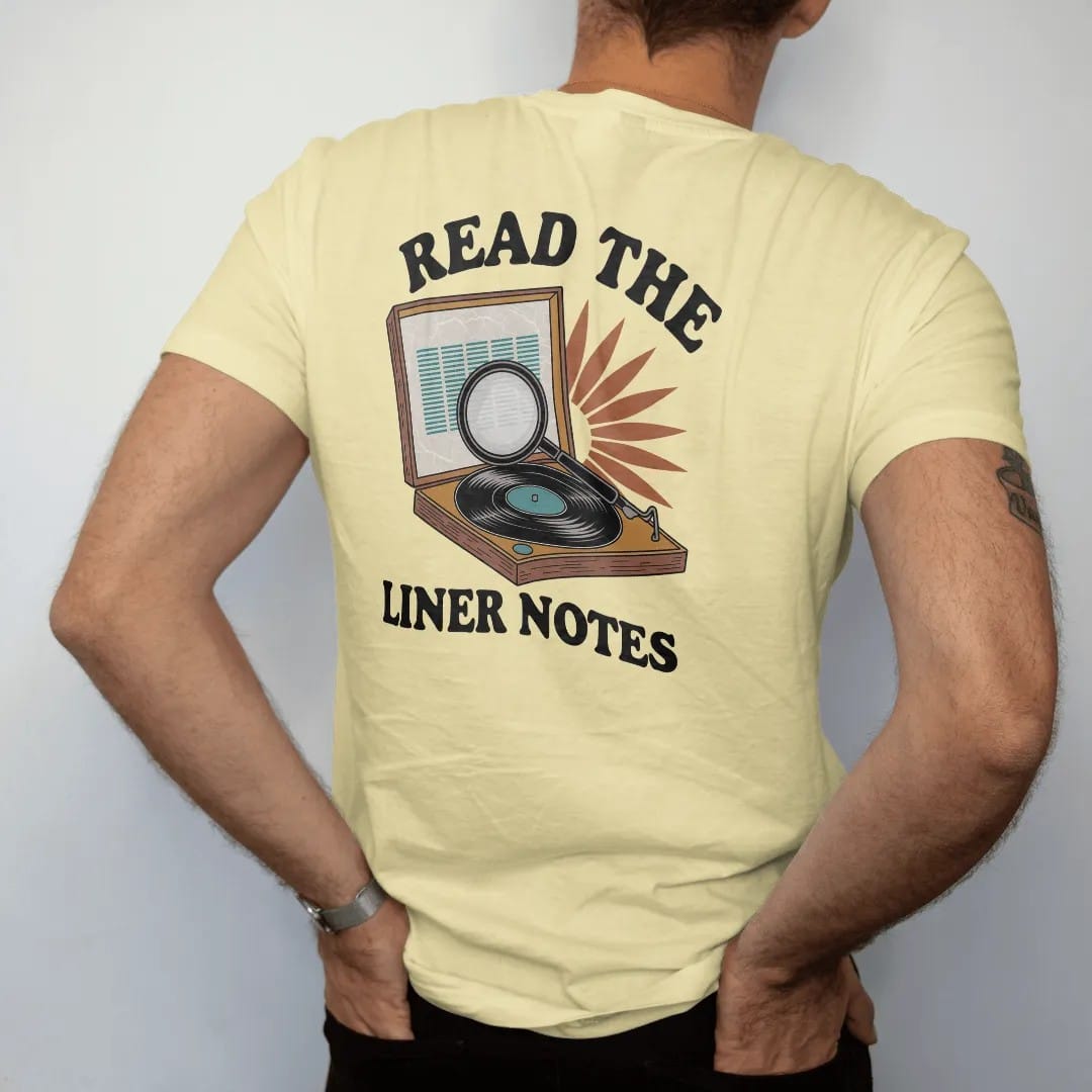 Man wearing a Butter tee, seen from the back: an open record sleeve under a magnifying glass with reading glasses, with "READ THE" and "LINER NOTES" in chunky 70s lettering and small 70s caps, printed in faded, cracked brown, burnt orange, faded…