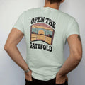 Man wearing a Bay tee, seen from the back: an opened gatefold album sleeve showing a desert landscape, with "OPEN THE" and "GATEFOLD" in chunky 70s lettering and small 70s caps, printed in faded, cracked brown, burnt orange, faded teal and mustard…