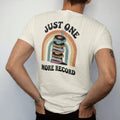 Man wearing a Ivory tee, seen from the back: a teetering stack of records with a tiny person adding one more, with "JUST ONE" and "MORE RECORD" in chunky 70s lettering and small 70s caps, printed in faded, cracked cream, mustard, burnt orange and…