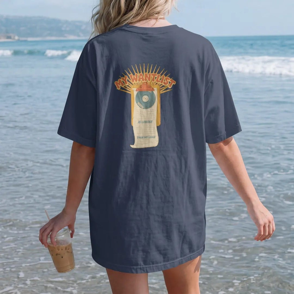 Woman on the beach in a Navy tee, back view: a long paper wantlist unrolling from a clipboard, with "MY WANTLIST", "IS LONGER" and "THAN MY LEASE" in chunky 70s lettering and small 70s caps, printed in faded, cracked cream, mustard, burnt orange…