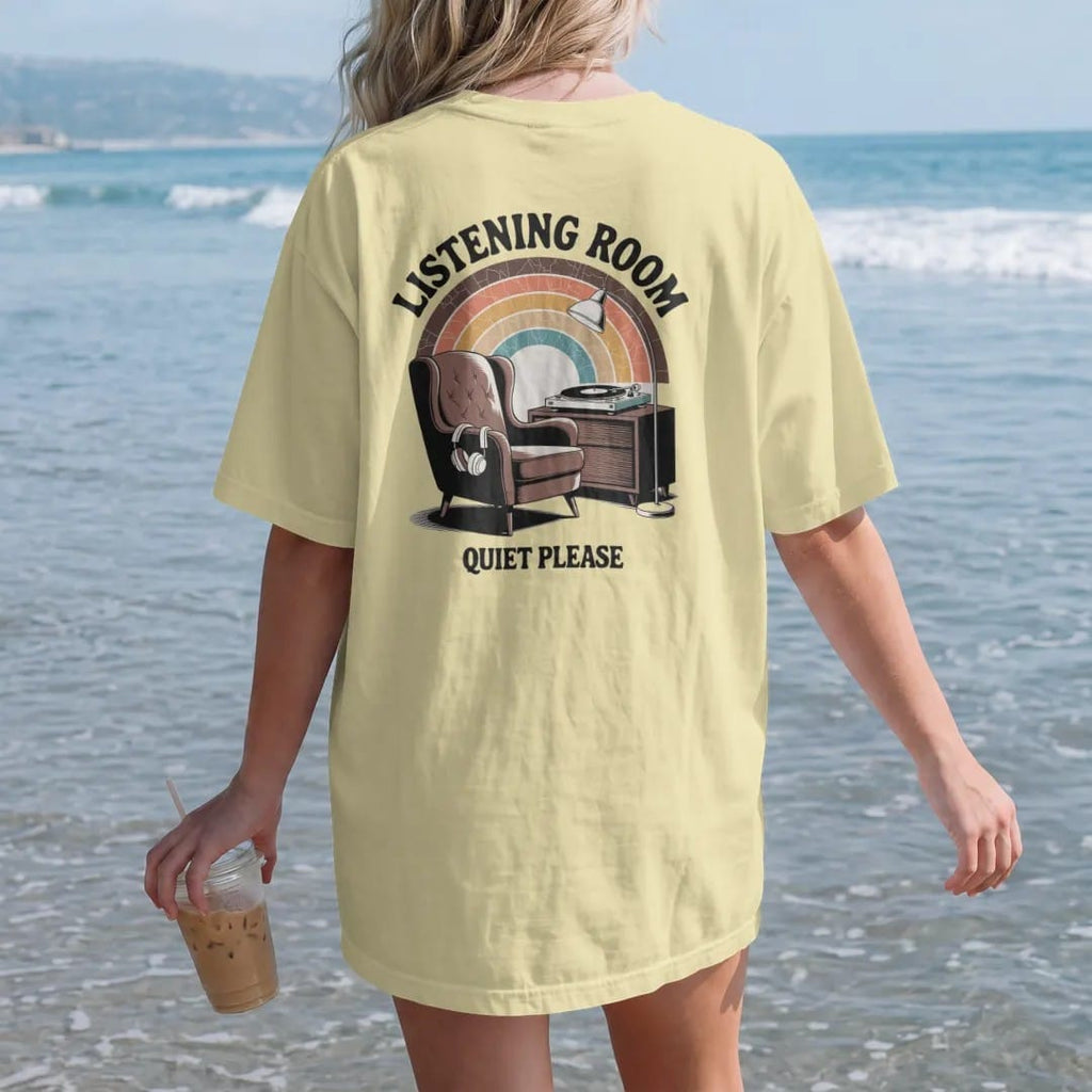 Woman on the beach in a Butter tee, back view: a mid-century armchair facing a turntable console with headphones, with "LISTENING ROOM" and "QUIET PLEASE" in chunky 70s lettering and small 70s caps, printed in faded, cracked brown, burnt orange,…