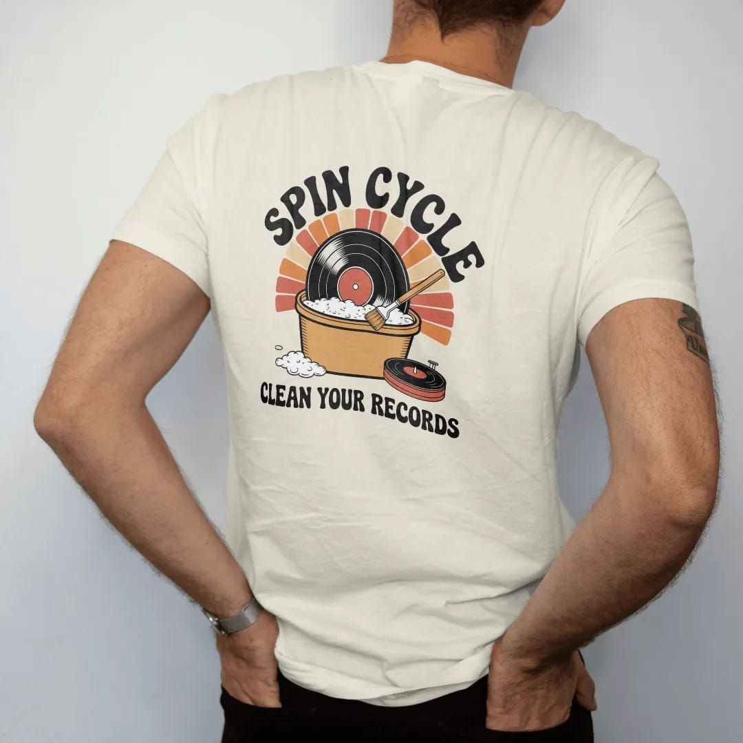 Man wearing a Ivory tee, seen from the back: a record in a bubble bath beside a cleaning-machine dial, with "SPIN CYCLE" and "CLEAN YOUR RECORDS" in chunky 70s lettering and small 70s caps, printed in faded, cracked cream, mustard, burnt orange and…