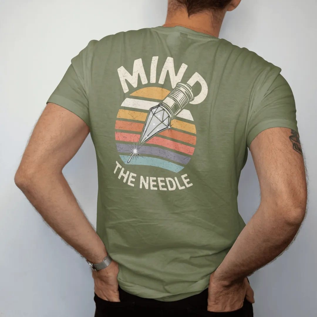 Man wearing a Moss tee, seen from the back: a huge diamond stylus tip drawn like a jewel, with "MIND" and "THE NEEDLE" in chunky 70s lettering and small 70s caps, printed in faded, cracked cream, mustard, burnt orange and faded teal over faded…