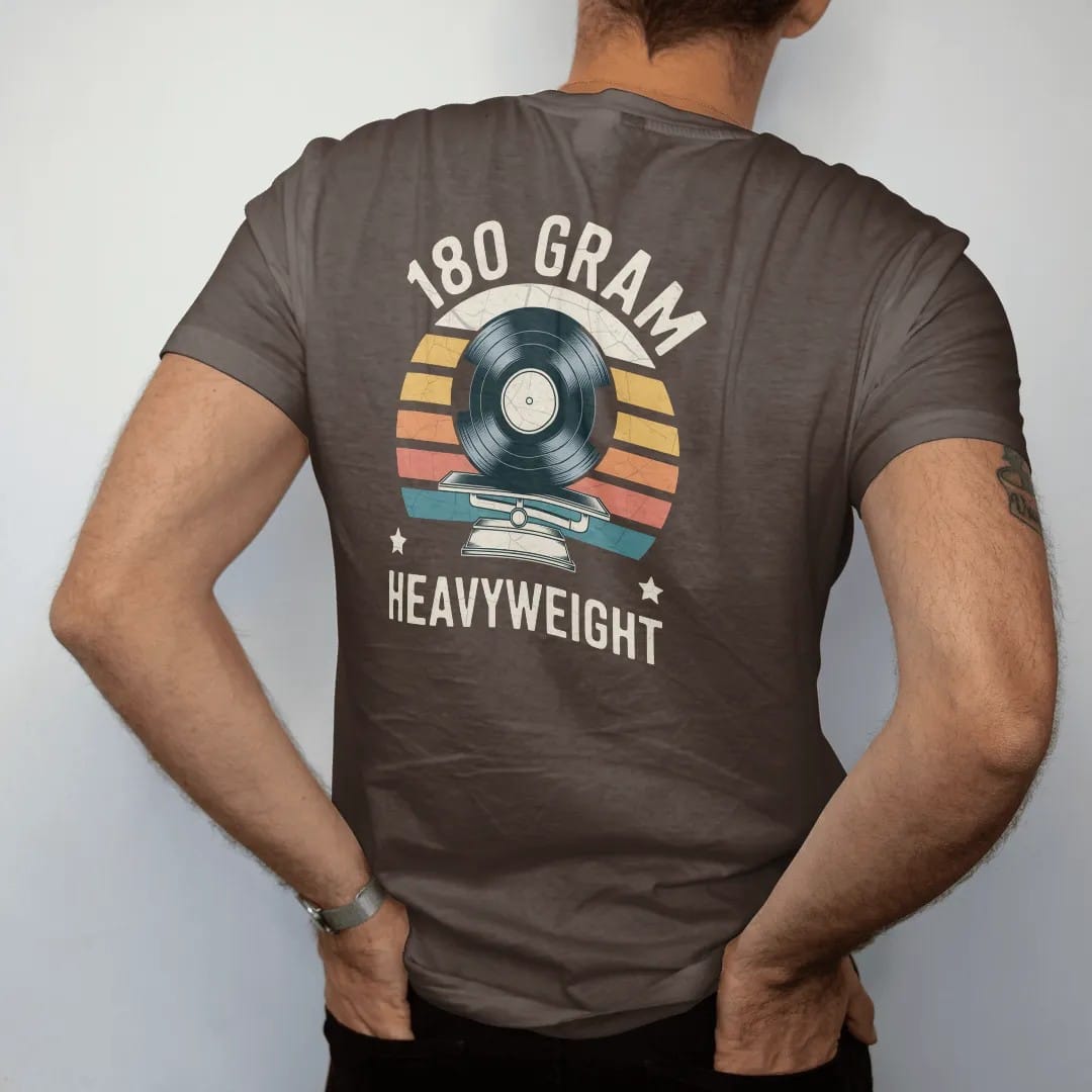 Man wearing a Espresso tee, seen from the back: a thick record on a balance scale like a prize fighter, with "180 GRAM" and "HEAVYWEIGHT" in chunky 70s lettering and small 70s caps, printed in faded, cracked cream, mustard, burnt orange and faded…