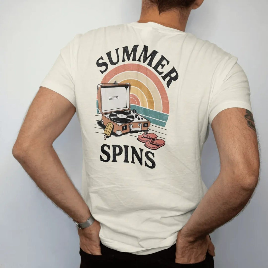 Man wearing a Ivory tee, seen from the back: a suitcase record player on a porch step with a record-shaped sunset, with "SUMMER SPINS" in chunky 70s lettering, printed in faded, cracked cream, mustard, burnt orange and faded teal over a faded…