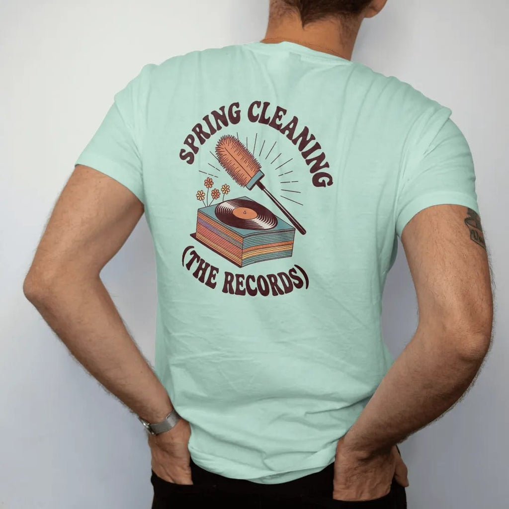 Man wearing a Chalky Mint tee, seen from the back: a feather duster and record brush over a stack sprouting spring flowers, with "SPRING CLEANING" and "(THE RECORDS)" in chunky 70s lettering and small 70s caps, printed in faded, cracked brown,…