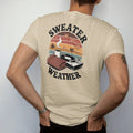 Man wearing a Sandstone tee, seen from the back: a mug, knit sweater and turntable among falling leaves, with "SWEATER WEATHER" and "SLOW SPINS" in chunky 70s lettering and small 70s caps, printed in faded, cracked brown, burnt orange, faded teal…