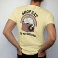 Man wearing a Butter tee, seen from the back: a fluffy cat asleep on top of a record bin, with "SHOP CAT" and "DO NOT DISTURB" in chunky 70s lettering and small 70s caps, printed in faded, cracked brown, burnt orange, faded teal and mustard over a…