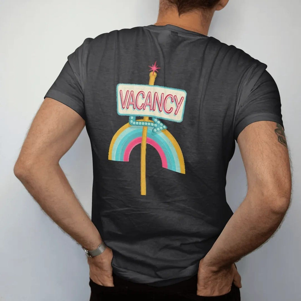 Man wearing a Black tee, seen from the back: a glowing neon vacancy sign on a pole with a bulb-dot arrow, with "VACANCY" in neon-tube script, printed in faded, cracked cream, mustard and turquoise with a neon pink accent over a faded rainbow arc.