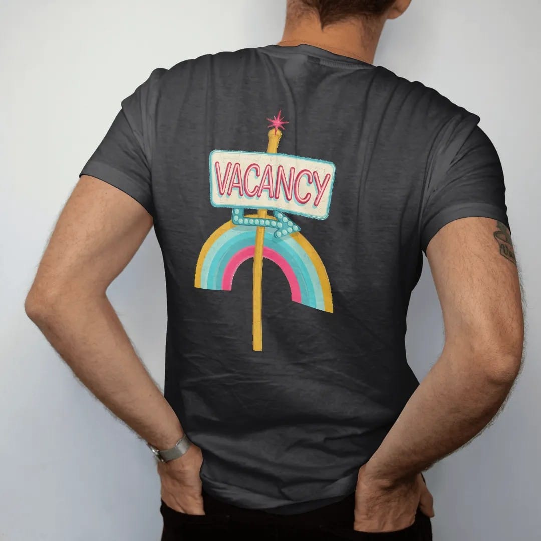 Man wearing a Black tee, seen from the back: a glowing neon vacancy sign on a pole with a bulb-dot arrow, with "VACANCY" in neon-tube script, printed in faded, cracked cream, mustard and turquoise with a neon pink accent over a faded rainbow arc.