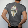 Man wearing a Graphite tee, seen from the back: an oversized diamond motel key fob with a brass key, with "ROOM 7" and "PLEASE RETURN KEY" in chunky 70s lettering and small 70s caps, printed in faded, cracked cream, mustard and turquoise with a…