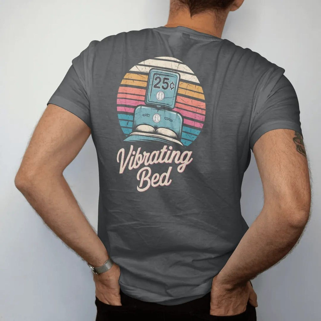 Man wearing a Graphite tee, seen from the back: a headboard coin box with a quarter dropping in, with "25¢" and "VIBRATING BED" in chunky 70s lettering and brush script, printed in faded, cracked cream, mustard and turquoise with a neon pink accent…