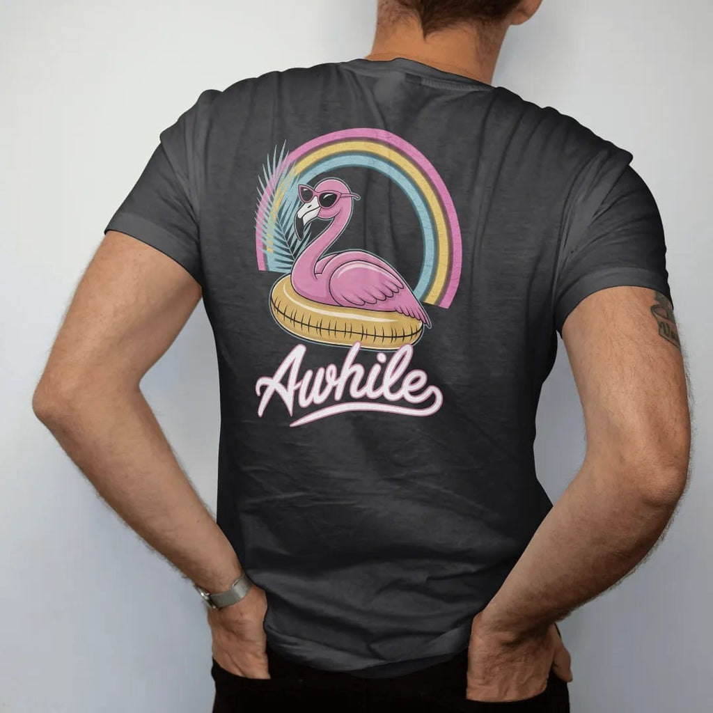 Man wearing a Black tee, seen from the back: a pink flamingo in sunglasses lounging on a pool float, with "STAY AWHILE" in neon-tube script, printed in faded, cracked cream, mustard and turquoise with a neon pink accent over a faded rainbow arc.