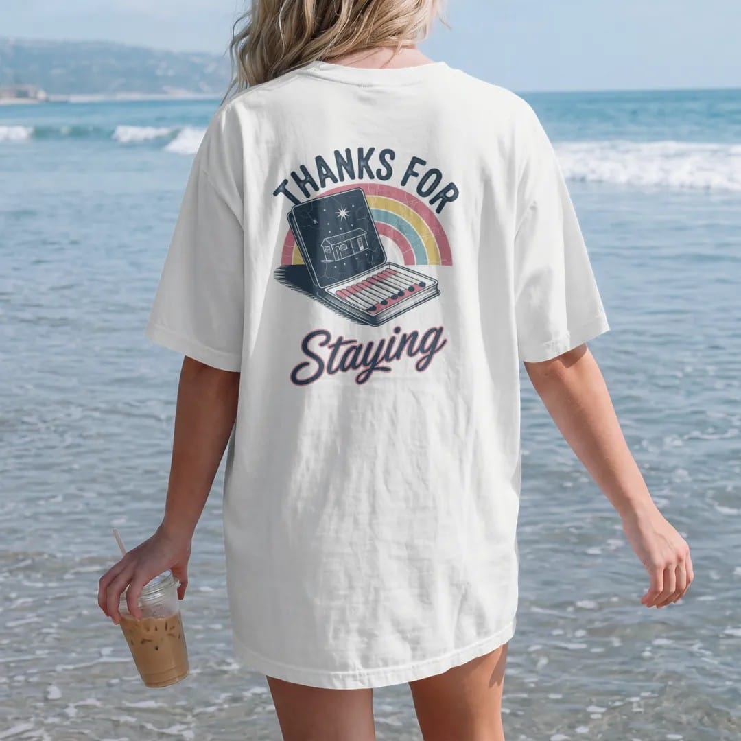 Woman on the beach in a White tee, back view: an open vintage motel matchbook with a motel drawing on the cover, with "THANKS FOR" and "STAYING" in chunky 70s lettering and brush script, printed in faded, cracked navy, rust red and dusty teal with…