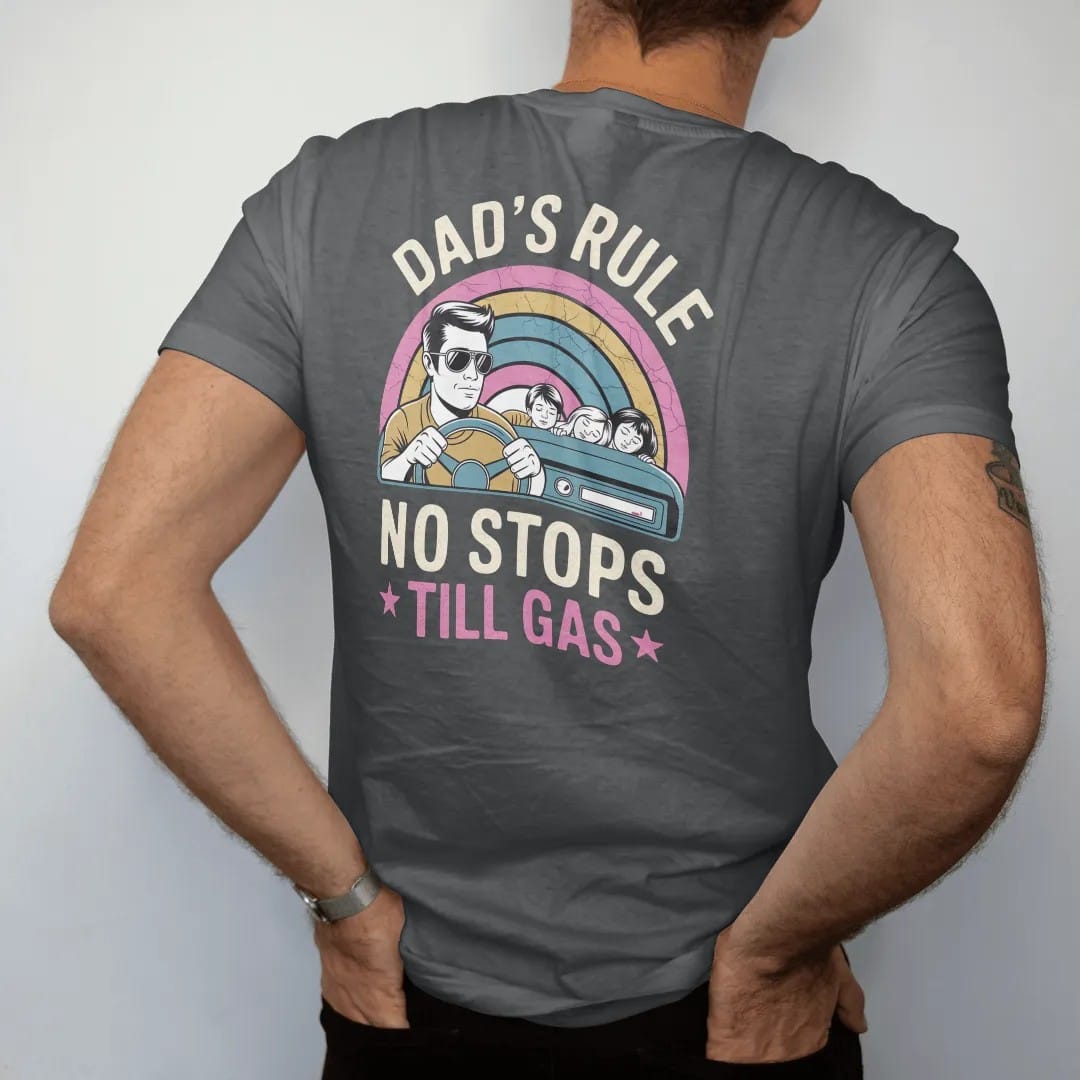 Man wearing a Graphite tee, seen from the back: a dad in aviators gripping the wheel beside a nearly full fuel gauge, with "DAD'S RULE", "NO STOPS" and "TILL GAS" in chunky 70s lettering and small 70s caps, printed in faded, cracked cream, mustard…