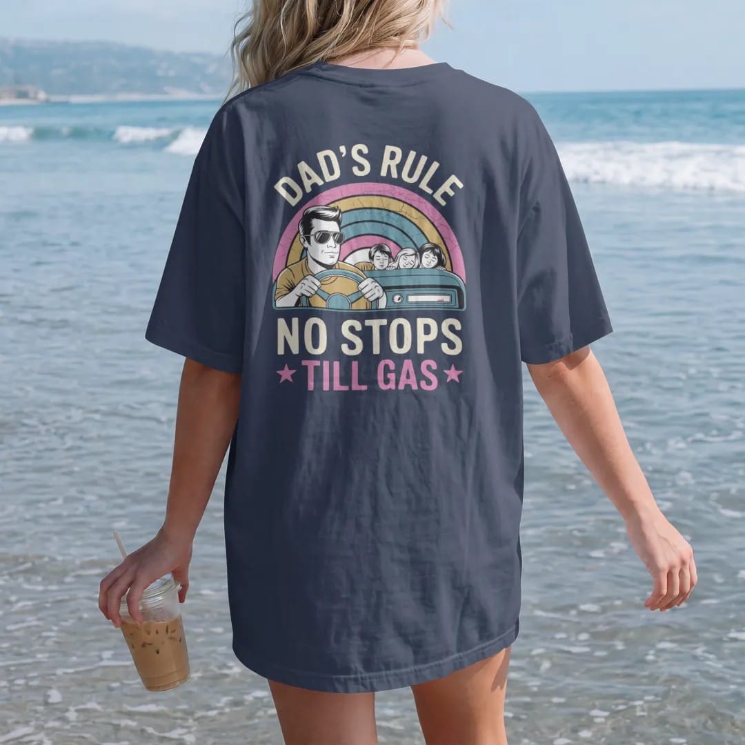 Woman on the beach in a Navy tee, back view: a dad in aviators gripping the wheel beside a nearly full fuel gauge, with "DAD'S RULE", "NO STOPS" and "TILL GAS" in chunky 70s lettering and small 70s caps, printed in faded, cracked cream, mustard and…
