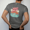 Man wearing a Pepper tee, seen from the back: a glowing motel pool at night reflecting a neon sign, with "NIGHT SWIM" in neon-tube script, printed in faded, cracked cream, mustard and turquoise with a neon pink accent over faded sunset stripes.