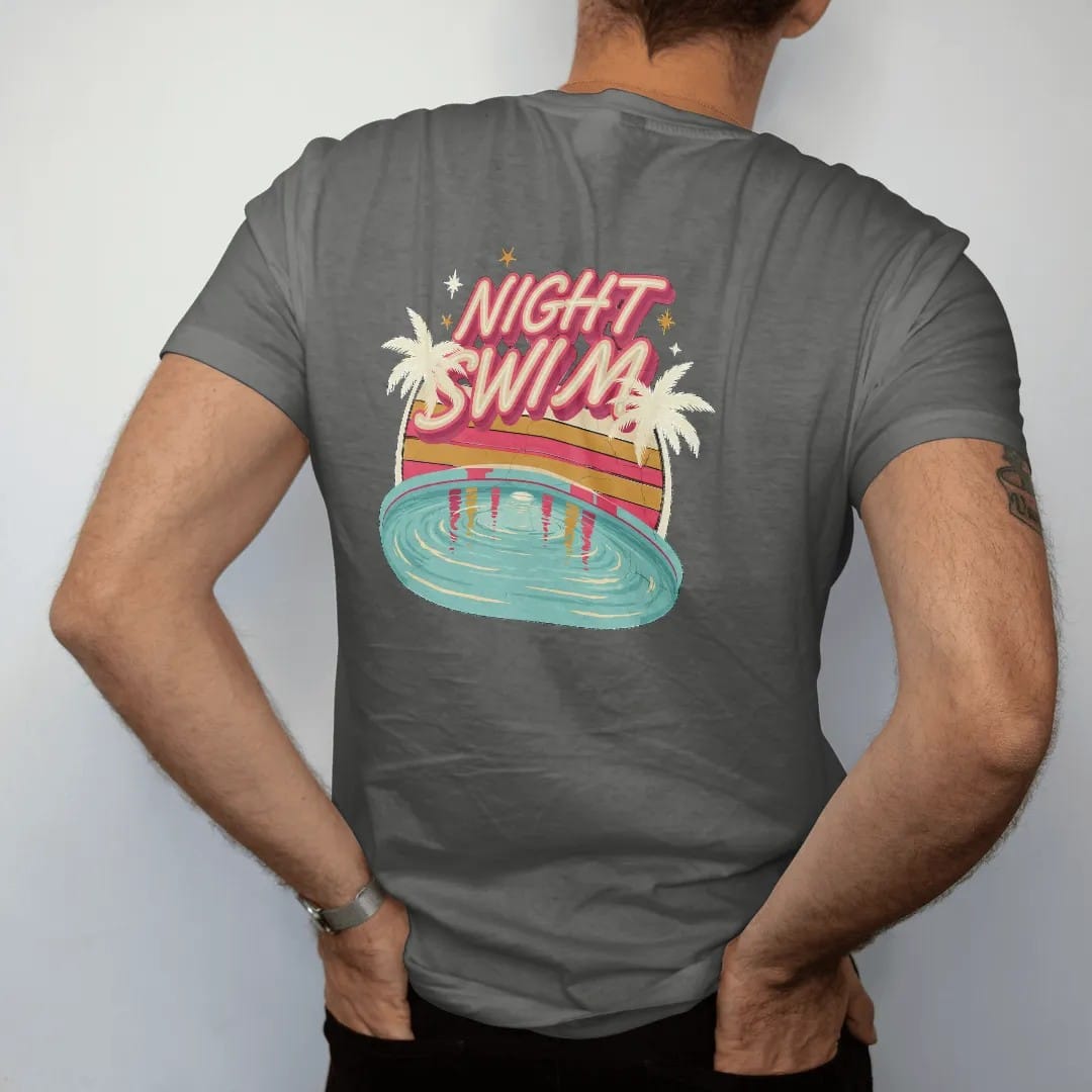 Man wearing a Pepper tee, seen from the back: a glowing motel pool at night reflecting a neon sign, with "NIGHT SWIM" in neon-tube script, printed in faded, cracked cream, mustard and turquoise with a neon pink accent over faded sunset stripes.