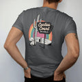 Man wearing a Graphite tee, seen from the back: a saguaro-shaped neon motel sign above adobe bungalows, with "CACTUS COURT" and "AIR COOLED" in neon-tube script and small 70s caps, printed in faded, cracked cream, mustard and turquoise with a neon…