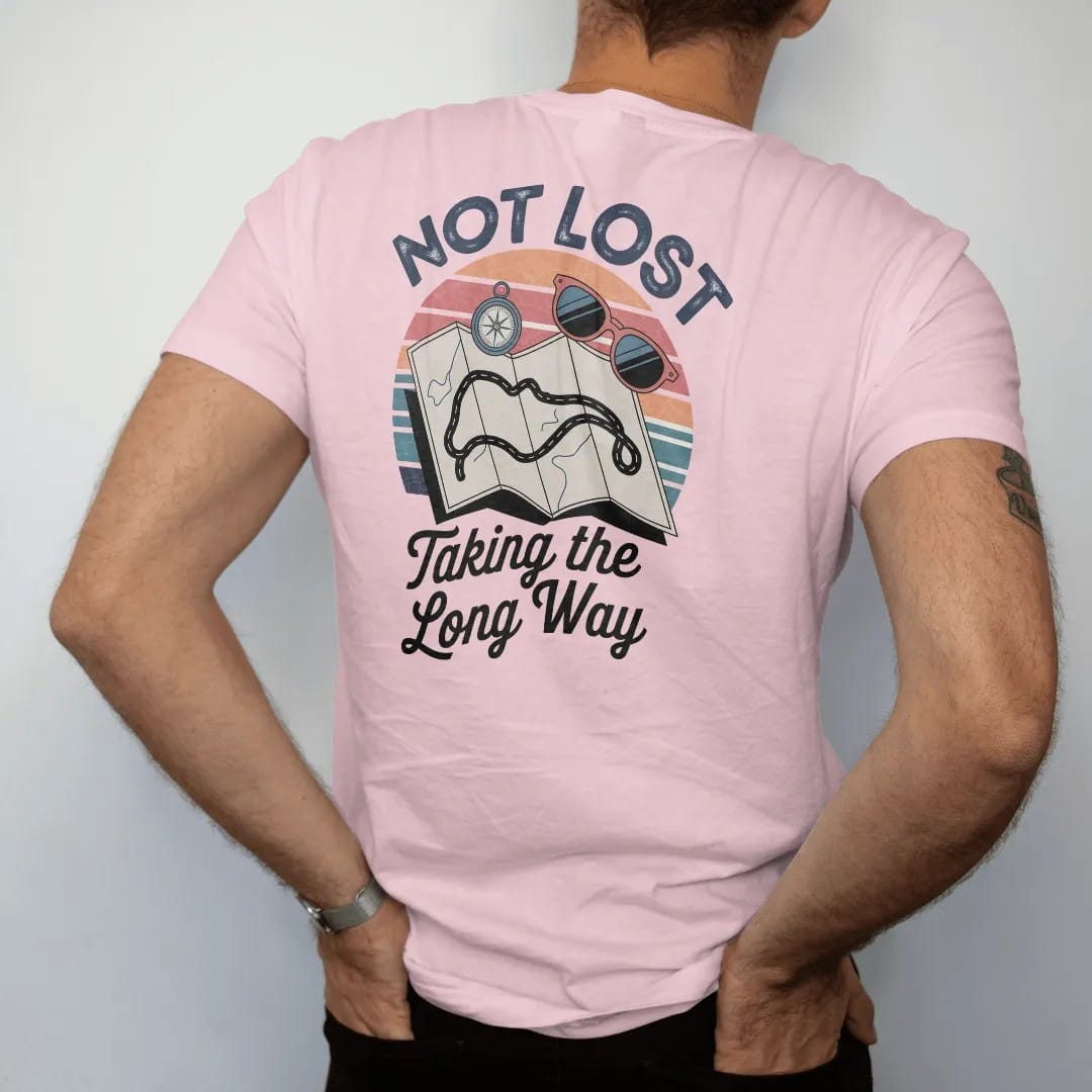 Man wearing a Blossom tee, seen from the back: an unfolded road map with a wobbly looping route, with "NOT LOST" and "TAKING THE LONG WAY" in chunky 70s lettering and brush script, printed in faded, cracked navy, rust red and dusty teal with a neon…