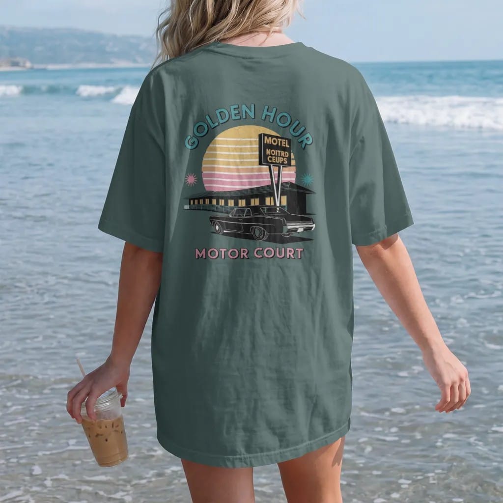 Woman on the beach in a Blue Spruce tee, back view: a motel row and tall sign silhouetted against a striped setting sun, with "GOLDEN HOUR" and "MOTOR COURT" in chunky 70s lettering and small 70s caps, printed in faded, cracked cream, mustard and…