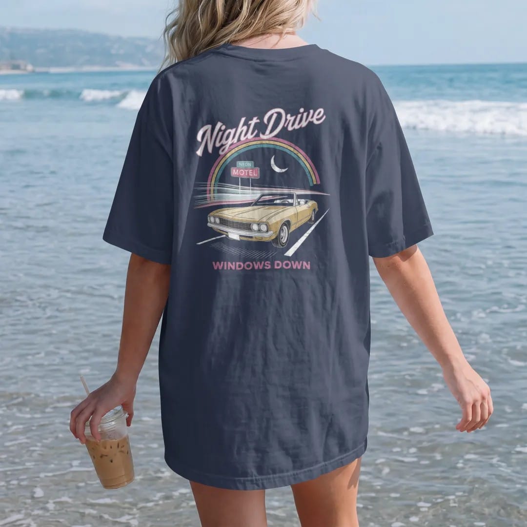 Woman on the beach in a Navy tee, back view: a convertible on a dark highway with neon streaks, with "NIGHT DRIVE" and "WINDOWS DOWN" in neon-tube script and small 70s caps, printed in faded, cracked cream, mustard and turquoise with a neon pink…