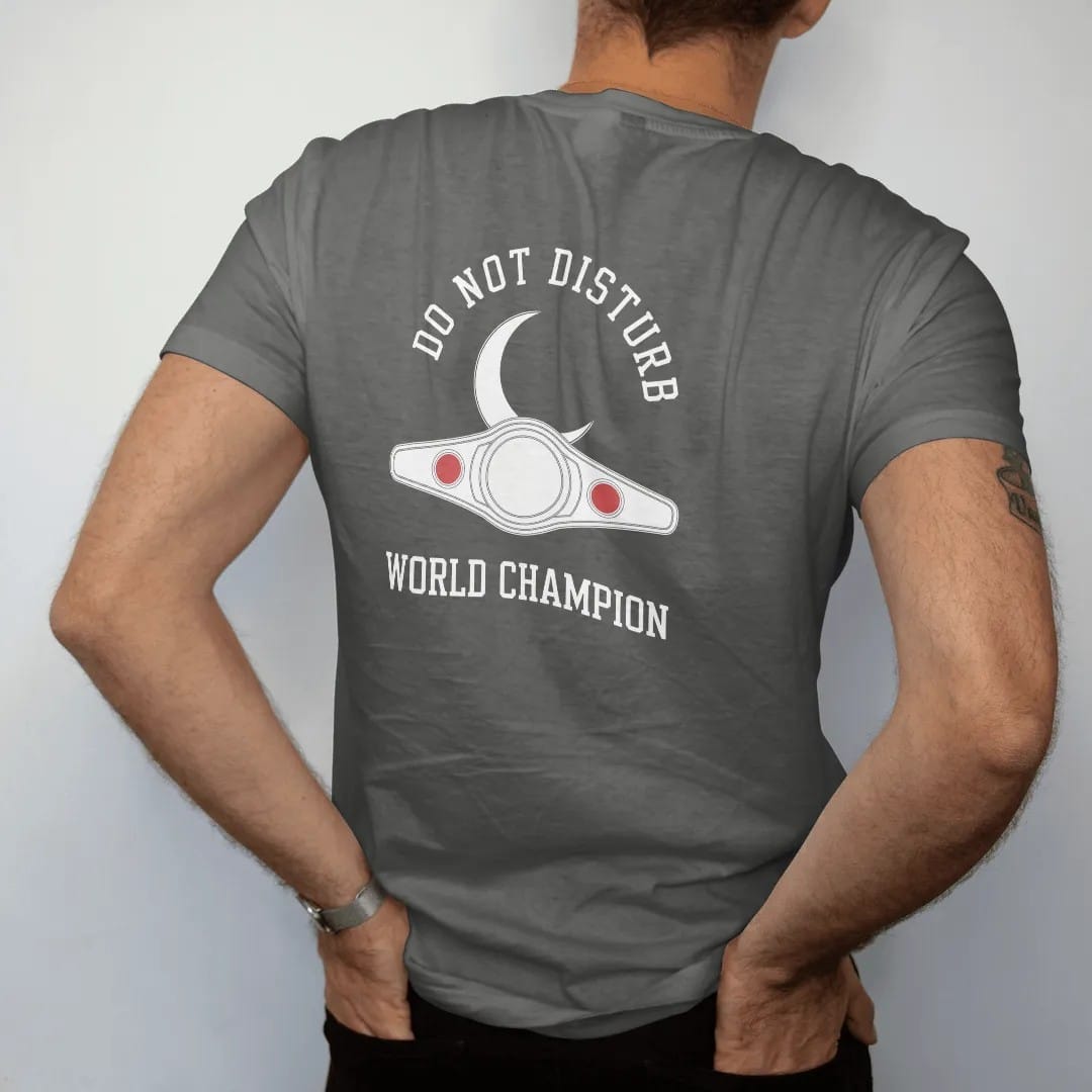 Man wearing a Pepper tee, seen from the back: minimal single-line drawing of a crescent moon resting on a slim outline championship belt, with "DO NOT DISTURB / WORLD CHAMPION" in small spaced-out caps, printed in bone white with a low-battery red…