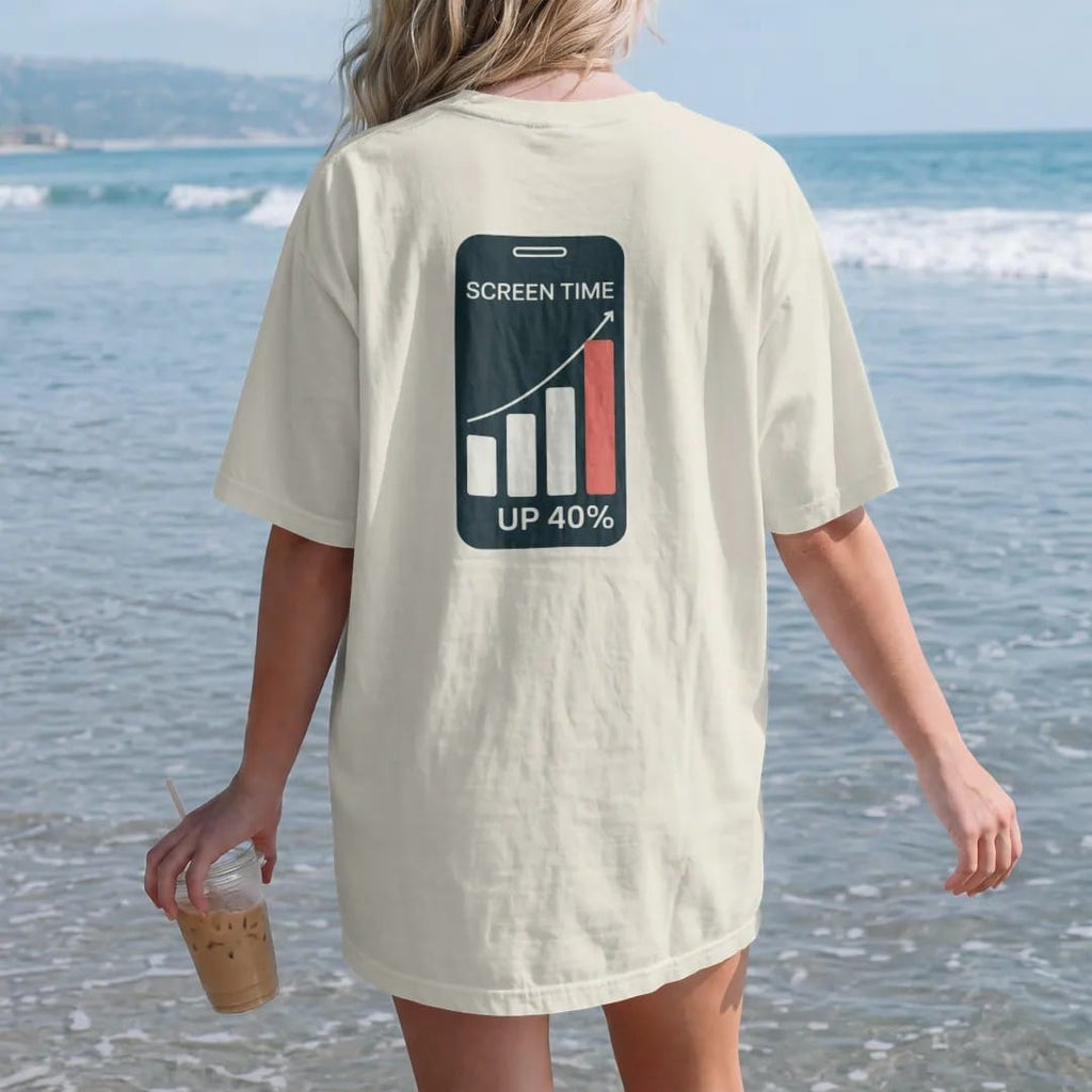 Woman on the beach in a Ivory tee, back view: minimal single-line drawing of a phone outline with a simple rising bar graph on the screen, with "SCREEN TIME / UP 40%" in small spaced-out caps, printed in bone white with a low-battery red accent on…