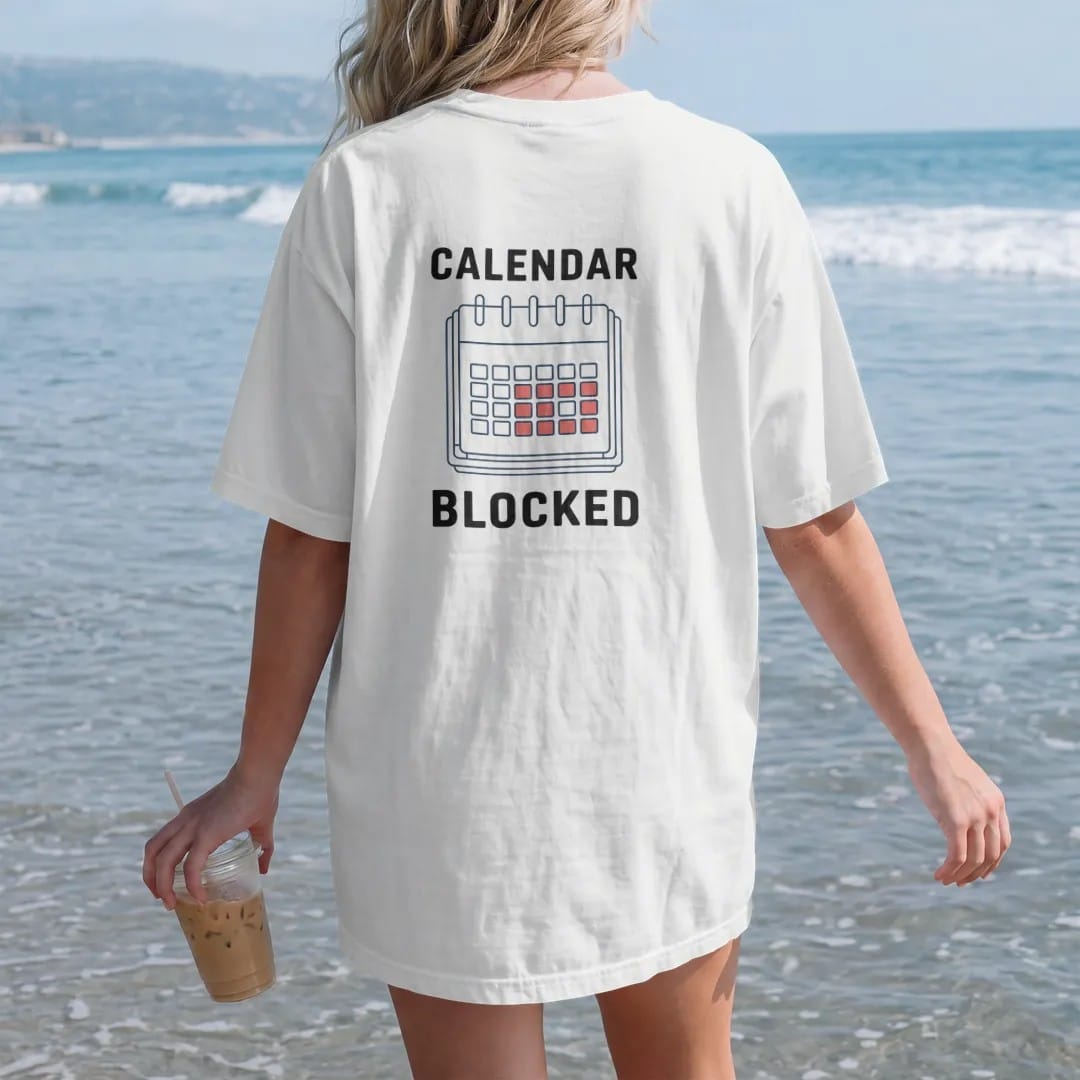 Woman on the beach in a White tee, back view: minimal single-line drawing of a calendar page outline with a small brick-wall pattern across it, with "CALENDAR / BLOCKED" in small spaced-out caps, printed in ink navy with a battery red accent on the…