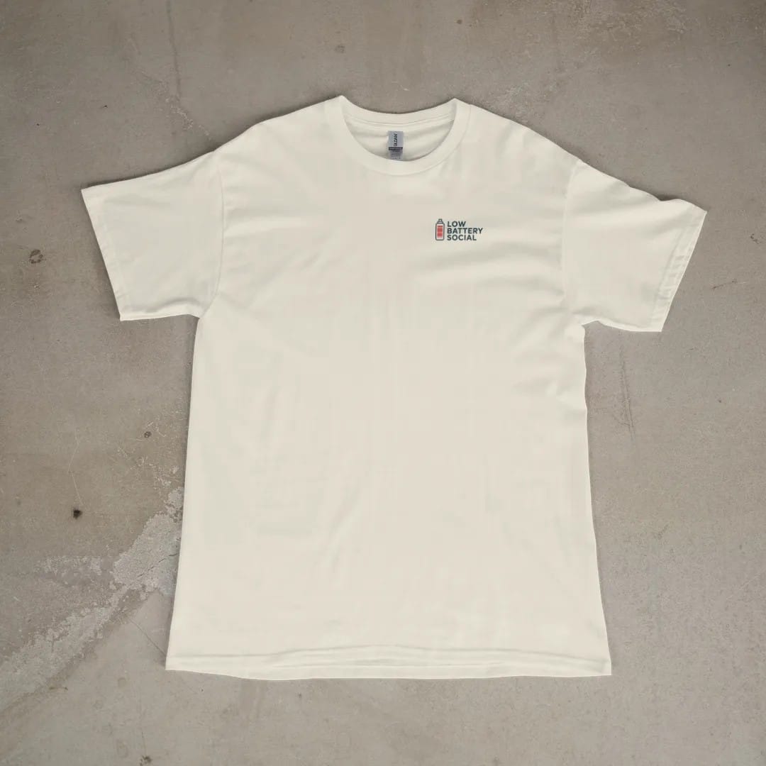 Front of a Ivory tee laid flat, with the small Low Battery Social logo on the left chest.