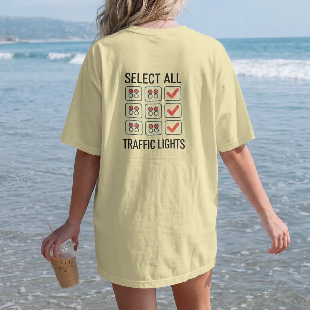 Woman on the beach in a Butter tee, back view: minimal single-line drawing of a thin 3-by-3 grid with small traffic lights in a few squares and checkmarks, with "SELECT ALL / TRAFFIC LIGHTS" in small spaced-out caps, printed in ink navy with a…